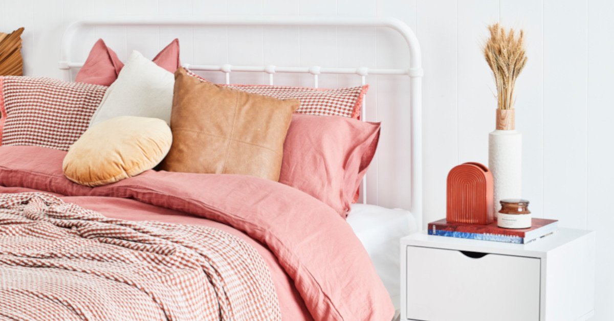 Bed with pink bedspread, next to white bedside with carefully arranged decor