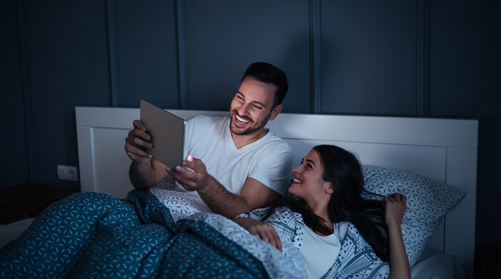 A couple sitting together and using their mobile devices in bed