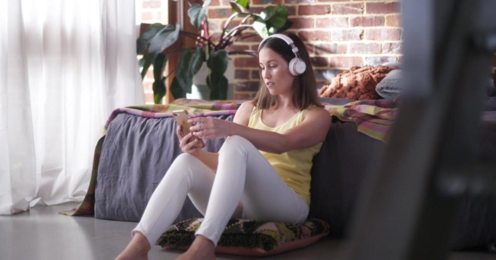 Women with headphones on sitting on the floor next to her bed, listening to music